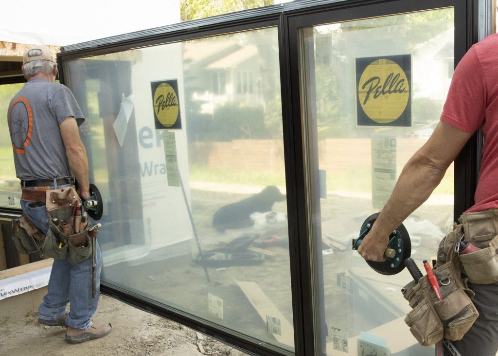 Two installers holding a glass panel using hand‑held vacuum suction cups.