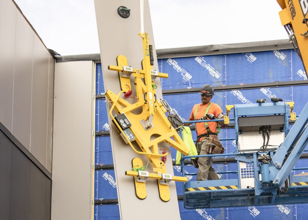 
Installers positioning insulated metal panels on a building façade using lifting equipment.